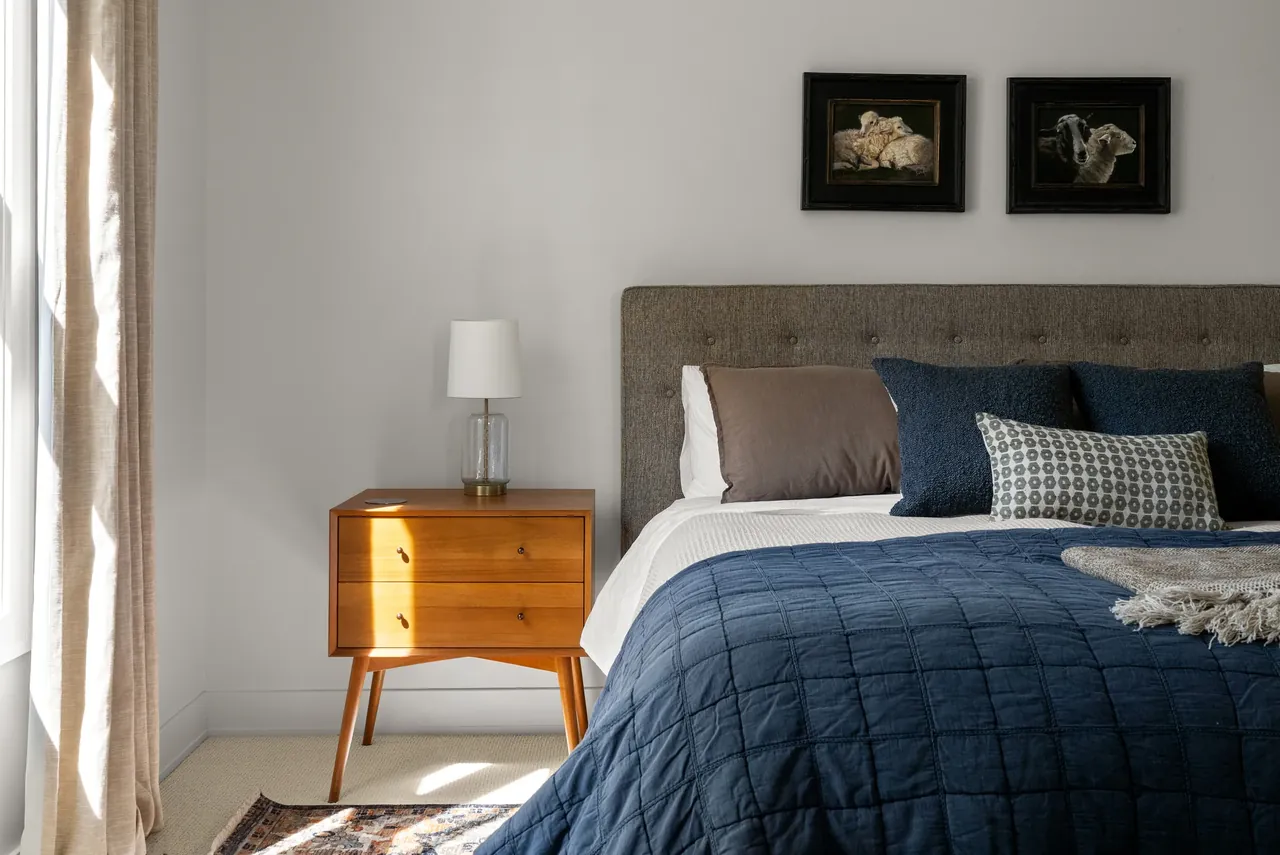 Bedroom with blue bedding, a dark upholstered headboard and bedside lamp