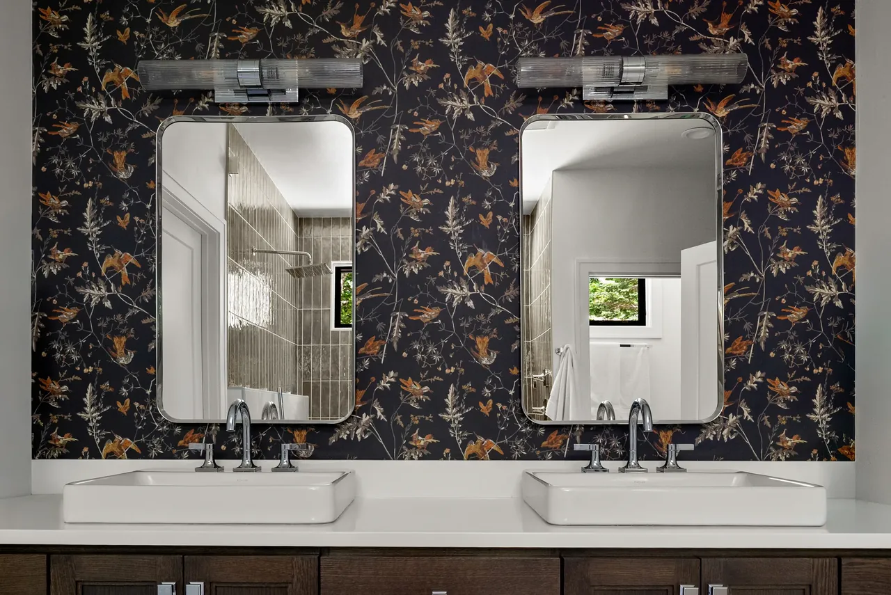 Double vanity with brass lighting and dark floral wallpaper