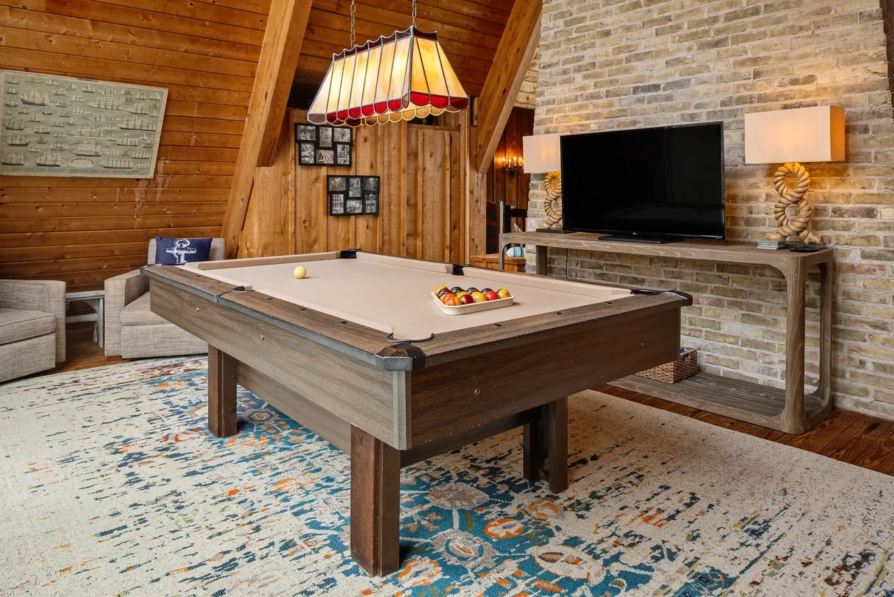 Timber-lined game room with a pool table and stone fireplace