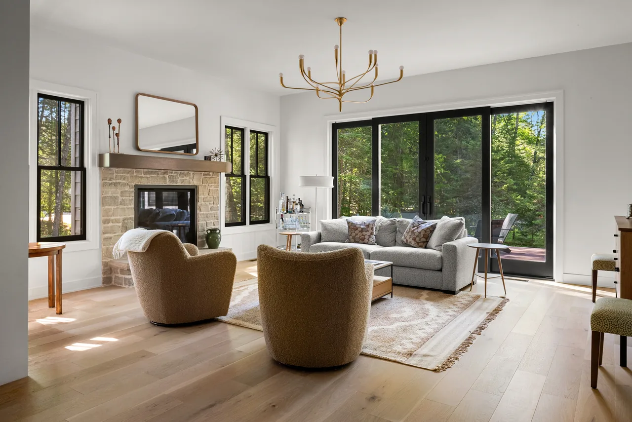 Light-filled living room with curved tan chairs and a wooded outlook